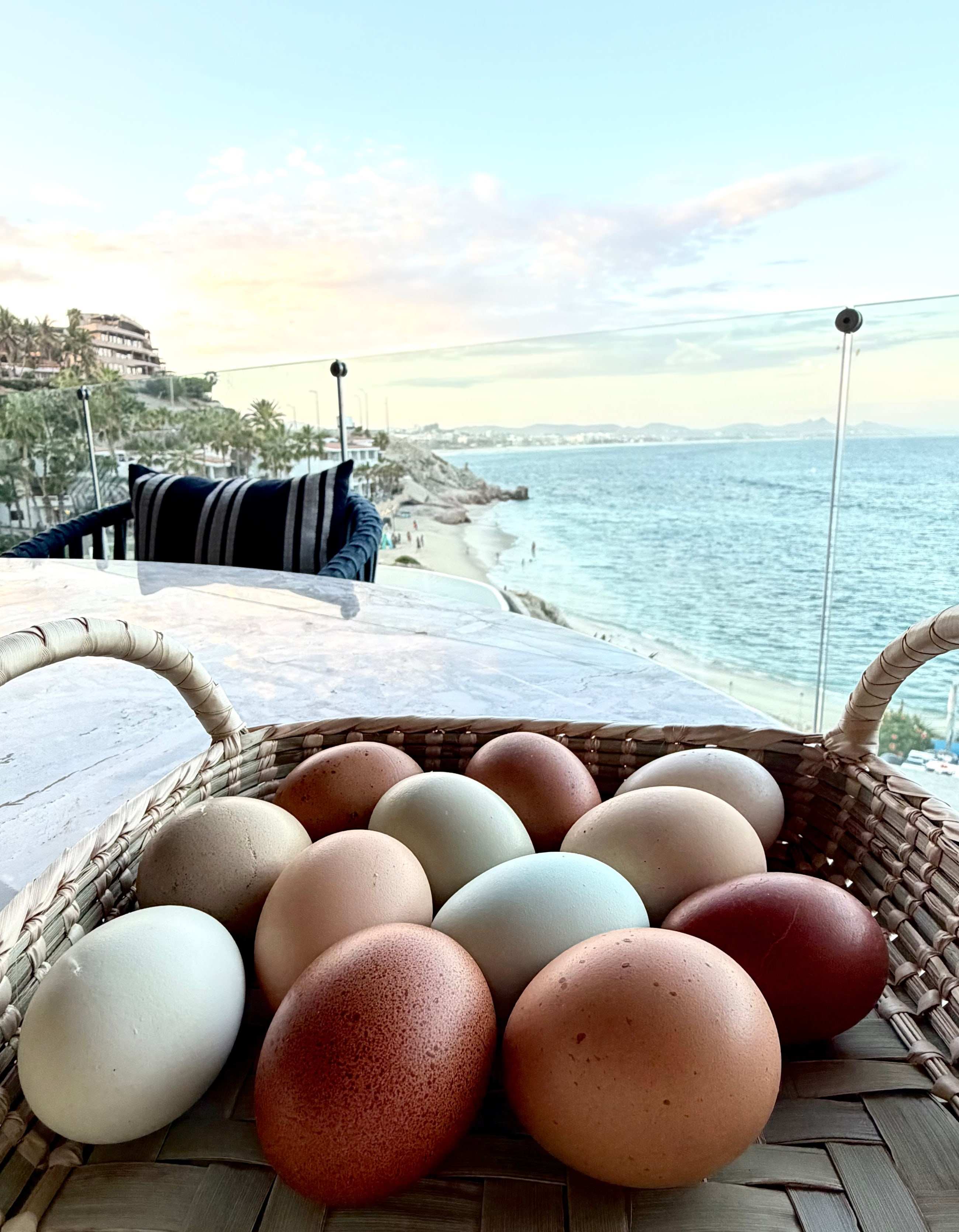A basket of Orchard eggs in shades of blue, cream and russet resting on marble above the Sea of Cortez at first light.